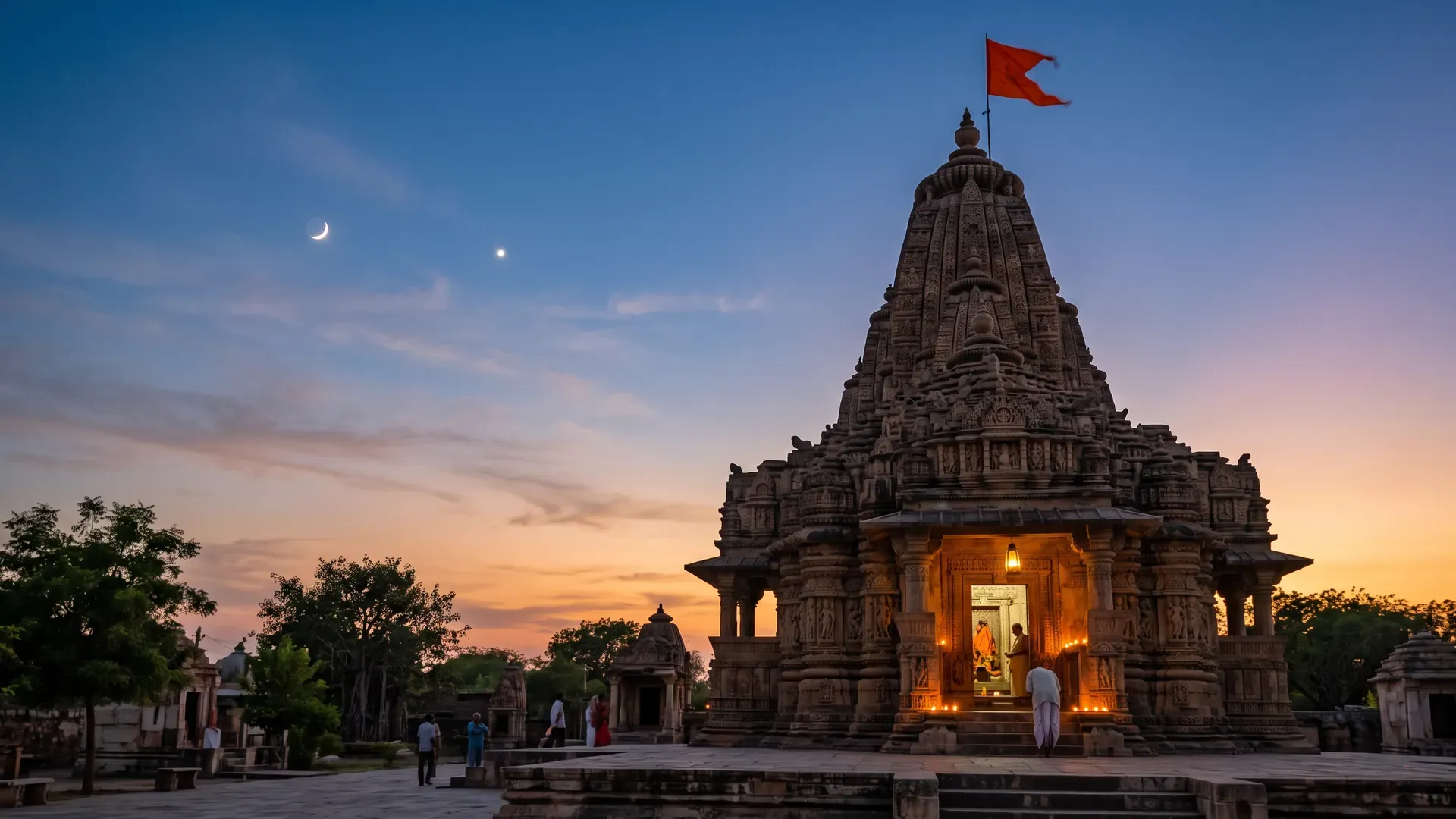 A thin crescent moon and a bright planet in the evening sky above an old stone temple lit with lamps